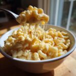 A fork lifting a cheesy portion of 3 ingredient stovetop mac and cheese from a white bowl.