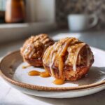 Two freshly baked apple pie cookies drizzled with caramel and icing on a plate.