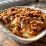 Close-up of a warm apple pie dump cake in a white dish, showing tender apple slices and a crumbly topping.