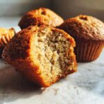 Close-up of a delicious banana protein muffin, with one muffin broken open to reveal its moist interior.
