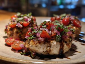 Close-up of perfectly cooked Bruschetta chicken topped with fresh tomatoes, red onion, and basil, drizzled with balsamic glaze.