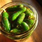 Close-up overhead view of whole candied jalapenos glistening in a glass jar.