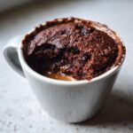 Close-up of a rich chocolate protein mug cake with a gooey center in a white mug.