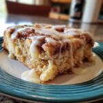 A close-up of a moist slice of cinnamon roll casserole, drizzled with sweet icing.
