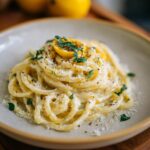 A close-up of a plate of Creamy Lemon Pasta, garnished with fresh parsley, grated cheese, and a lemon slice.