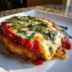 A close-up of a delicious slice of crispy Eggplant Parmesan, topped with marinara sauce, melted mozzarella, and fresh basil.