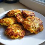 A close-up of several golden-brown zucchini fritters piled on a white plate, showcasing their crispy texture.