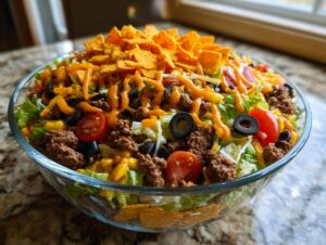 A large glass bowl filled with a colorful Dorito Taco Salad, topped with crushed Doritos, cheese, and dressing.