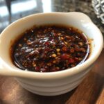 Close-up of a white bowl filled with flavorful 4-ingredient dumpling sauce, featuring chili flakes and spices.
