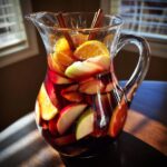 A clear glass pitcher filled with delicious fall sangria, featuring slices of apples, oranges, and cinnamon sticks.