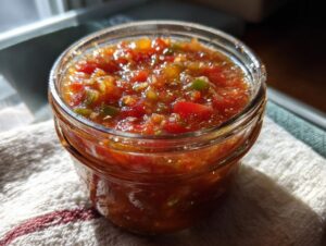 Close-up of a jar filled with vibrant Fresh Tomato Canned Salsa, showing chunks of tomatoes and peppers.
