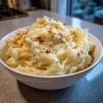A close-up of a white bowl filled with creamy garlic parmesan mashed potatoes, topped with crispy garlic bits.