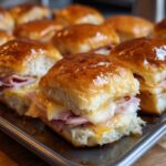 Close-up of a tray of golden-brown Ham and Cheese Sliders, with melted cheese oozing out.