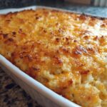 Close-up of a golden-brown baked hashbrown casserole with melted cheese topping in a white baking dish.
