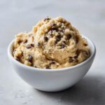 A white bowl filled with creamy high protein cookie dough studded with chocolate chips.