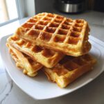 A stack of golden-brown high protein waffles on a white plate, ready to be served.