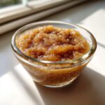 A close-up shot of a glass bowl filled with glistening homemade applesauce, sprinkled with cinnamon.