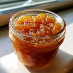 Close-up of a small glass jar filled with glistening, amber-colored pear preserves.