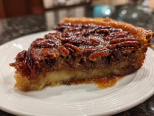 A close-up of a slice of pecan pie dump cake on a white plate, showcasing the gooey pecan topping and cake base.