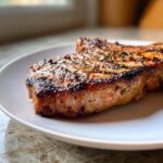 A perfectly grilled pork chop showcasing grill marks and herbs, prepared with a delicious marinade for pork chops.