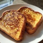 Two golden-brown slices of protein french toast dusted with cinnamon on a white plate.