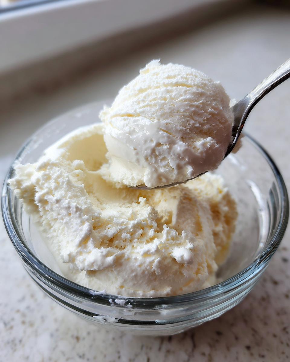 A spoonful of creamy protein ice cream being lifted from a glass bowl.