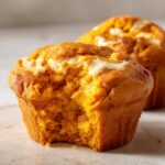 A close-up of a Starbucks pumpkin cream cheese muffin with a bite taken out, showing the moist interior and cream cheese swirl.