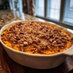 A golden-brown sweet potato casserole topped with a crunchy pecan streusel in a white baking dish.
