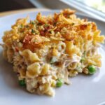 A close-up of a serving of creamy tuna casserole with noodles, peas, and a crispy fried onion topping.