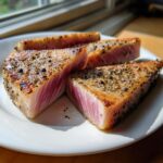 Four juicy tuna steaks seasoned with pepper, seared to perfection and served on a white plate.