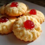 Close-up of delicious whipped shortbread cookies topped with bright red cherries.