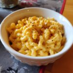 A close-up of a white bowl filled with creamy 5 ingredient slow cooker mac and cheese, topped with black pepper.