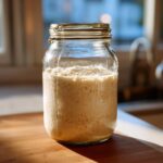 A bubbly, active sourdough starter in a glass jar, showing signs of fermentation.