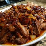 Close-up of tender, shredded apple cider braised pork shoulder with onions in a rich sauce.
