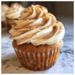 Close-up of a delicious apple pie cupcake topped with creamy cinnamon frosting and a sprinkle of cinnamon.
