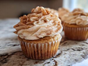 Close-up of a delicious apple pie cupcake topped with swirled cinnamon frosting and a sprinkle of cinnamon.