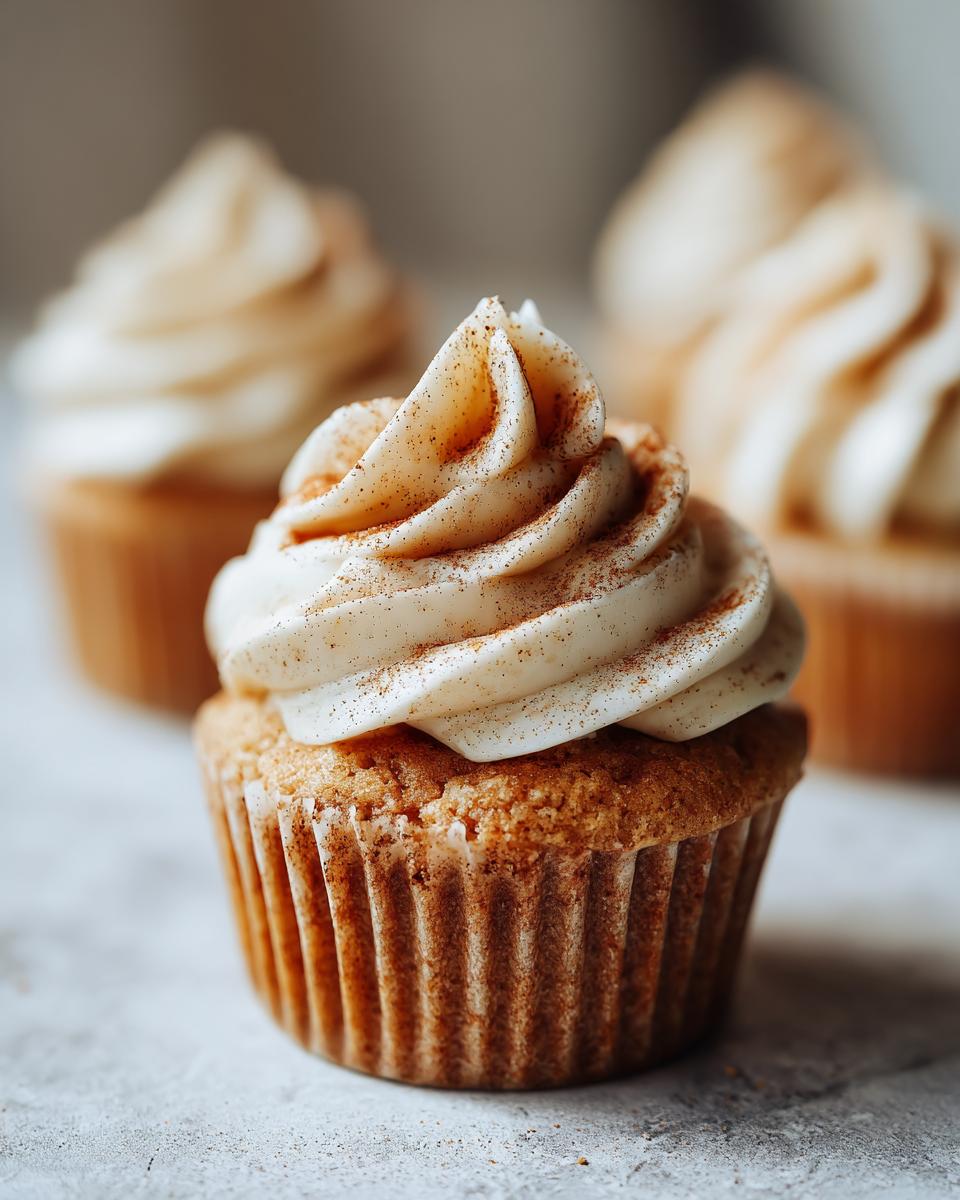 Close-up of a delicious apple pie cupcake topped with swirled cinnamon frosting and a sprinkle of cinnamon.
