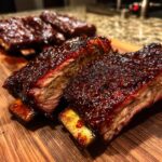 Close-up of tender Asian beef short ribs glazed with a dark, glossy sauce on a wooden board.