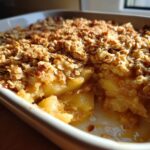 Close-up of a freshly baked apple crisp in a white dish, showing tender baked apples under a golden brown oat topping.