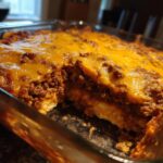 A close-up view of a freshly baked beef enchilada casserole in a glass baking dish, topped with melted cheddar cheese.