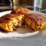 Close-up of golden-brown canned salmon patties on a white plate, one split open to show flaky texture.