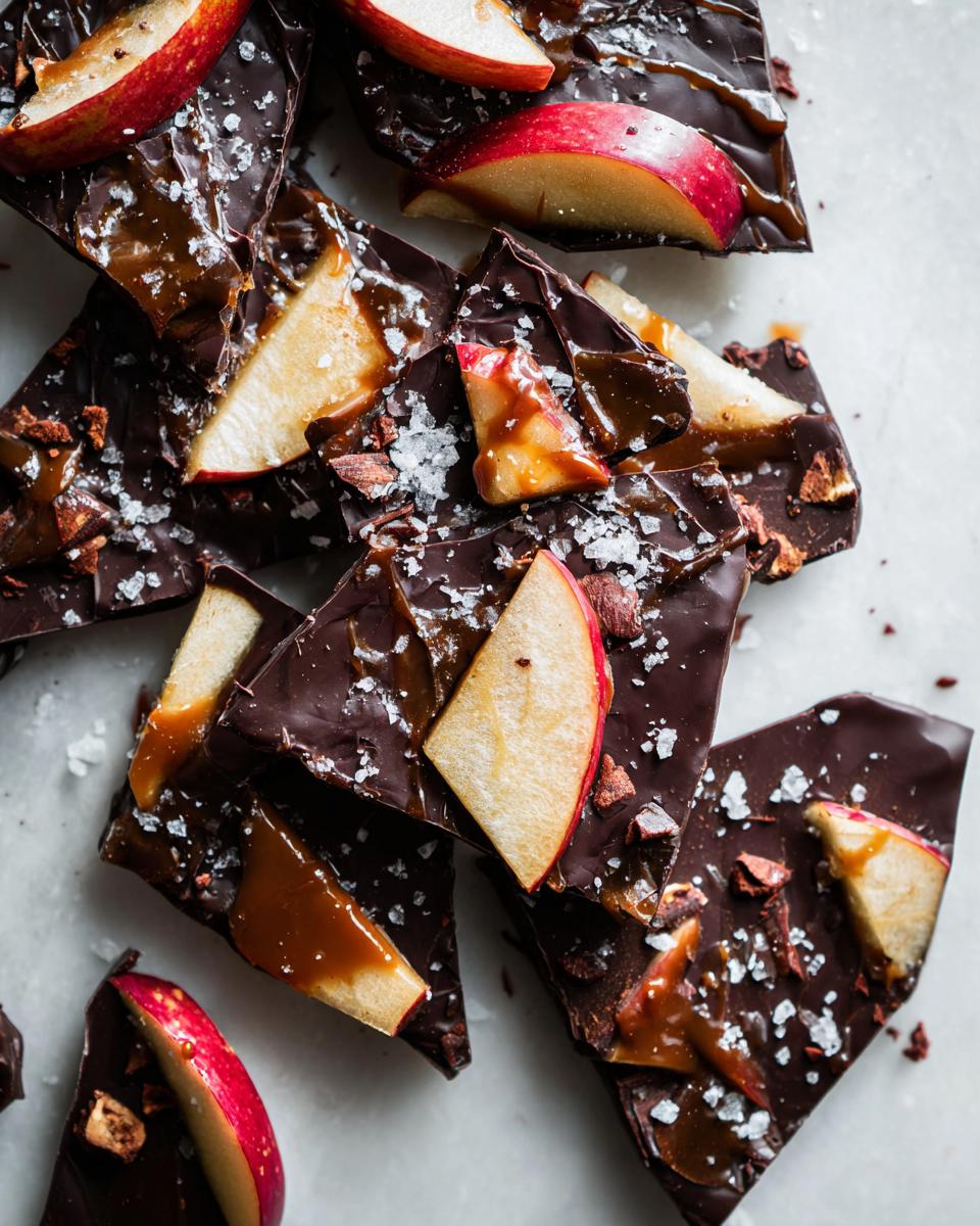 Close-up of broken pieces of dark chocolate caramel apple bark topped with apple slices and sea salt.