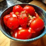 Close-up of a blue bowl filled with fresh cherry tomato salsa, chopped onions, and herbs.