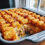 A close-up of a baked Chicken Bacon Ranch Tater Tot Casserole in a baking dish, showing crispy tater tots, melted cheese, and bacon.
