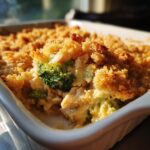 Close-up of a freshly baked chicken broccoli casserole in a white baking dish, featuring a golden crispy topping and visible chunks of chicken and broccoli.