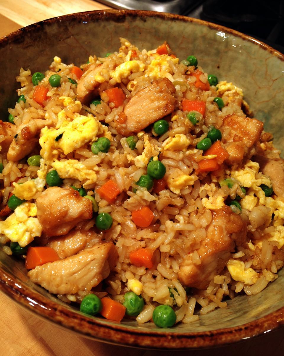 A close-up of a bowl filled with homemade Chicken Fried Rice, featuring tender chicken pieces, scrambled eggs, peas, and diced carrots.