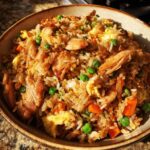 A close-up of a bowl filled with savory chicken fried rice, featuring tender chicken pieces, scrambled eggs, peas, and carrots.