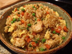 A close-up of a bowl filled with flavorful chicken fried rice, featuring tender chicken pieces, peas, carrots, and scrambled egg.