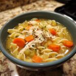 A close-up of a comforting bowl of chicken noodle soup, featuring shredded chicken, egg noodles, and carrots.