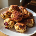 A close-up of golden-brown cranberry turkey stuffing balls piled on a white plate.